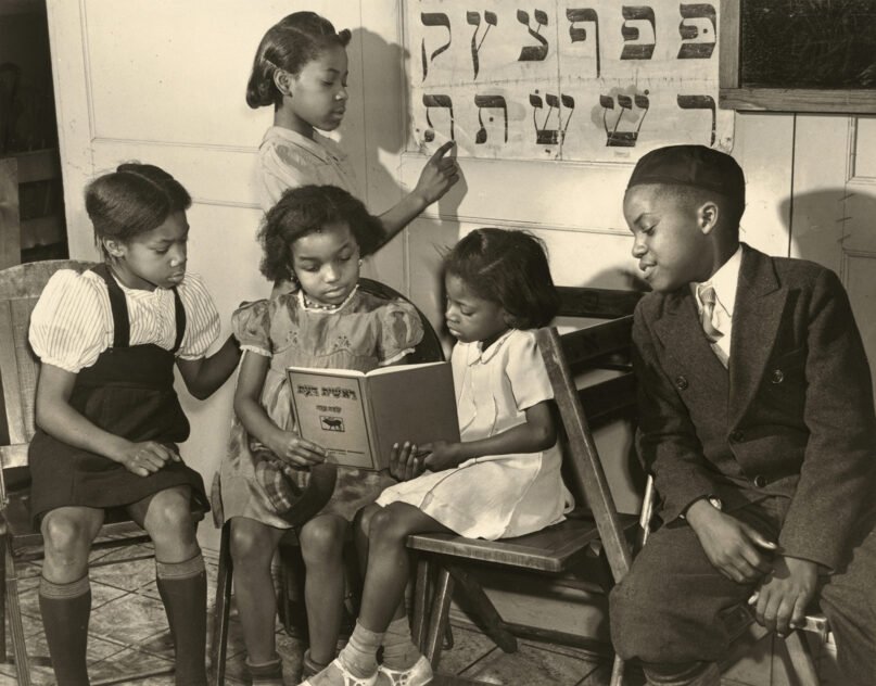 Young Black children read out of a book written in Hebrew in 1940 in Harlem, New York. Another girl studies a Hebrew alphabet. From the series: The Commandment Keepers: African American Jewish Congregation in Harlem. (Collection of the Smithsonian National Museum of African American History and Culture, © Alexander Alland Jr.)