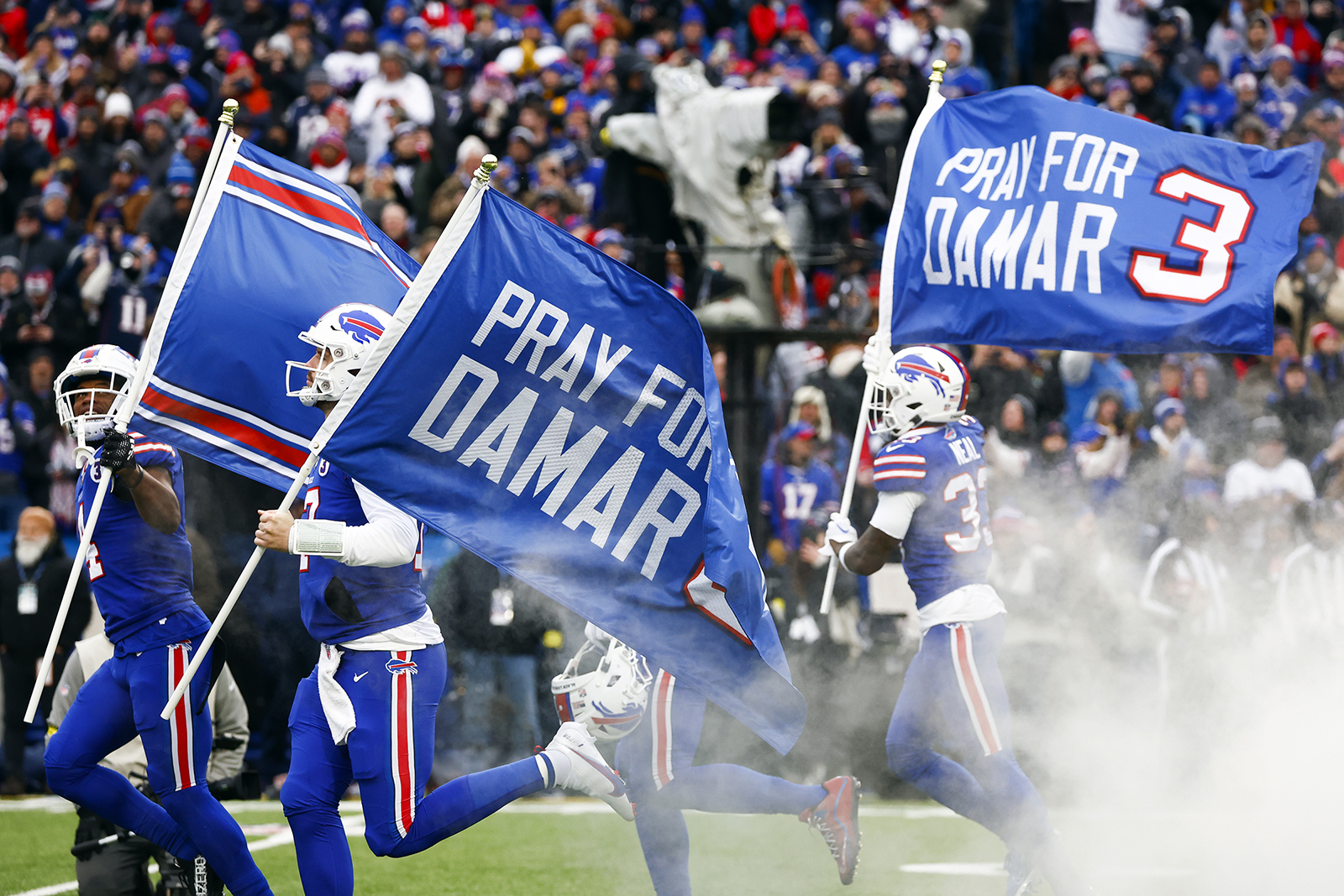 The Buffalo Bills carry flags onto the field reading "Pray for Damar" in support of safety Damar Hamlin before an NFL football game against the New England Patriots, Sunday, Jan. 8, 2023, in Orchard Park, N.Y. Hamlin remains hospitalized after suffering a catastrophic on-field collapse in the team's previous game against the Cincinnati Bengals. (AP Photo/Jeffrey T. Barnes)