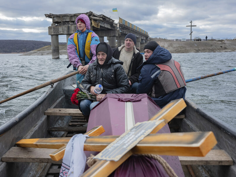 A woman sits in a boat crossing the Siverskyi-Donets River near Staryi-Saltiv, Kharkiv region, Ukraine, Jan. 4, 2023, transporting the coffin containing her dead son, a Ukrainian soldier who was killed in fighting with Russians. (AP Photo/Erik Marmor)