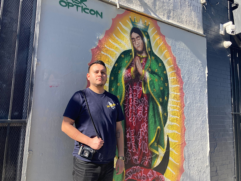 Oscar Rodriguez Zapata poses with a Virgin of Guadalupe painting in Boyle Heights in Los Angeles that he was photographing, Satuday, Jan. 21, 2023. RNS photo by Alejandra Molina
