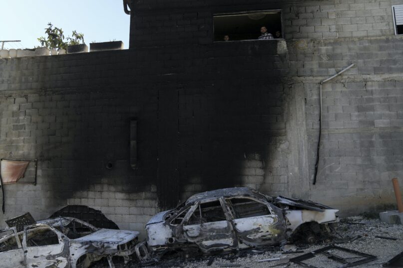Palestinians look out from a damaged building next to scorched cars in the town of Hawara, near the West Bank city of Nablus, on Feb. 27, 2023. (AP Photo/Nasser Nasser)