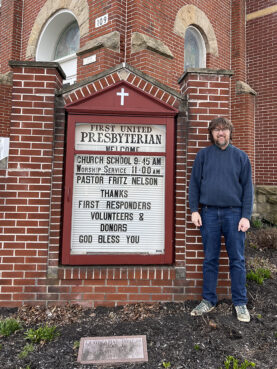 Pastor Fritz Nelson poses next to a sign thanking first reponders, volunteers and donors at First United Presbyterian Church in East Palestine, Ohio, Tuesday, March 21, 2023. RNS photo by Kathryn Post
