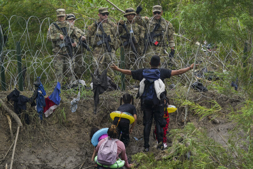 A migrant gestures to Texas National Guard members standing behind razor wire on the bank of the Rio Grande, seen from Matamoros, Mexico, May 11, 2023. Pandemic-related U.S. asylum restrictions, known as Title 42, are set to expire May 11. (AP Photo/Fernando Llano)