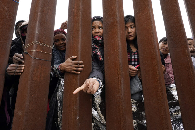 Migrants reach through a border wall for clothing handed out by volunteers, as they wait between two border walls to apply for asylum, Friday, May 12, 2023, in San Diego. (AP Photo/Gregory Bull)