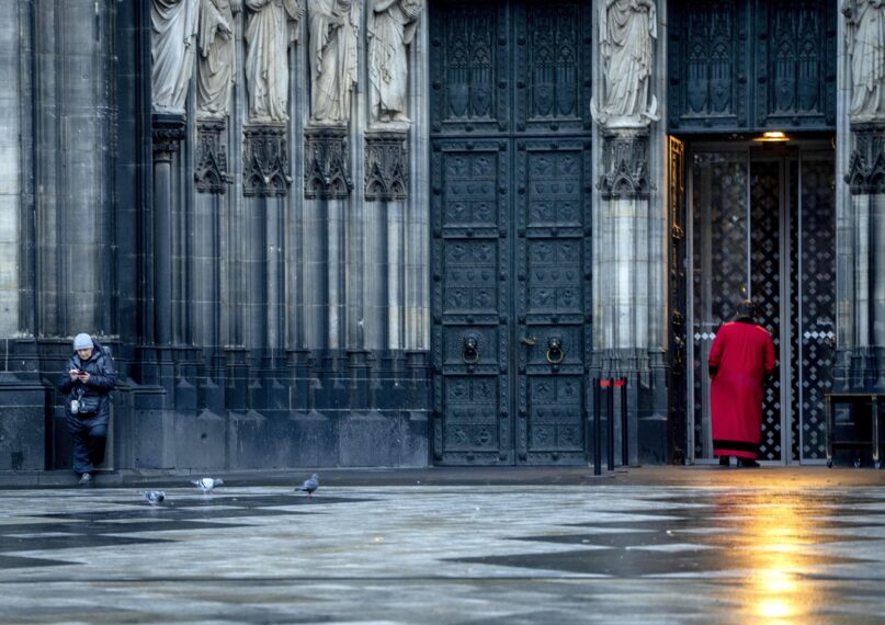 FILE - A cathedral door keeper and a woman wait in front of the Cathedral in Cologne, Germany, on Nov. 30, 2022. A court on Tuesday, June 13, 2023, ordered a German diocese to pay 300,000 euros ($323,000) in compensation to a man who was repeatedly abused by a Catholic priest in the 1970s, a ruling that a victims' association said was the first of its kind in Germany. The state court in Cologne ruled in a case in which the plaintiff, a man now aged 62 who was abused more than 300 times by a priest, had sought 750,000 euros from the Cologne archdiocese, German news agency dpa reported. (AP Photo/Michael Probst)