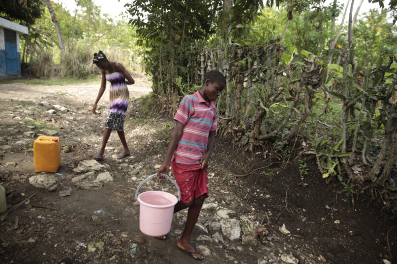 Siblings Mylouise Veillard, left, and Myson walk home with water they collected from a well, for cooking, cleaning and drinking, in a rural area of Saint-Louis-du-Sud, Haiti, Thursday, May 25, 2023. The siblings were considered “poverty orphans
