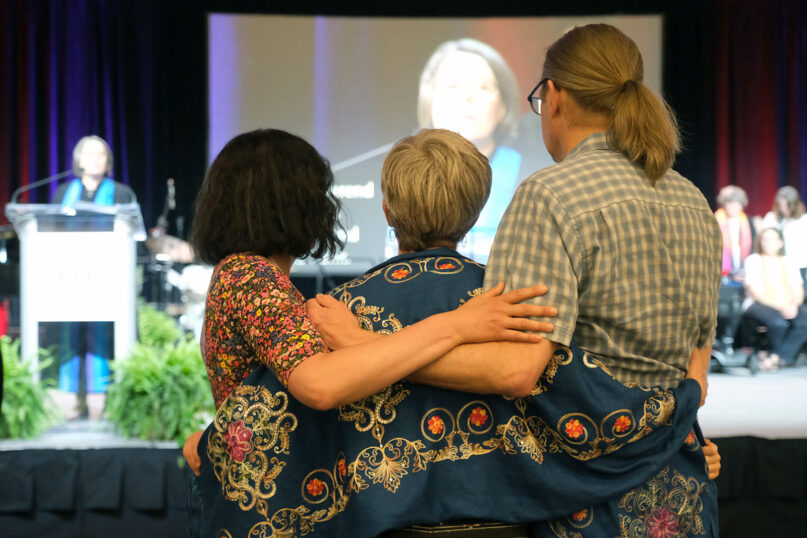 A family embraces while listening to the roll call of those religious professionals who died in the past year during the Unitarian Universalist Association General Assembly, Thursday, June 22, 2023, in Pittsburgh, Pennsylvania. Photo © 2023 Nancy Pierce/UUA