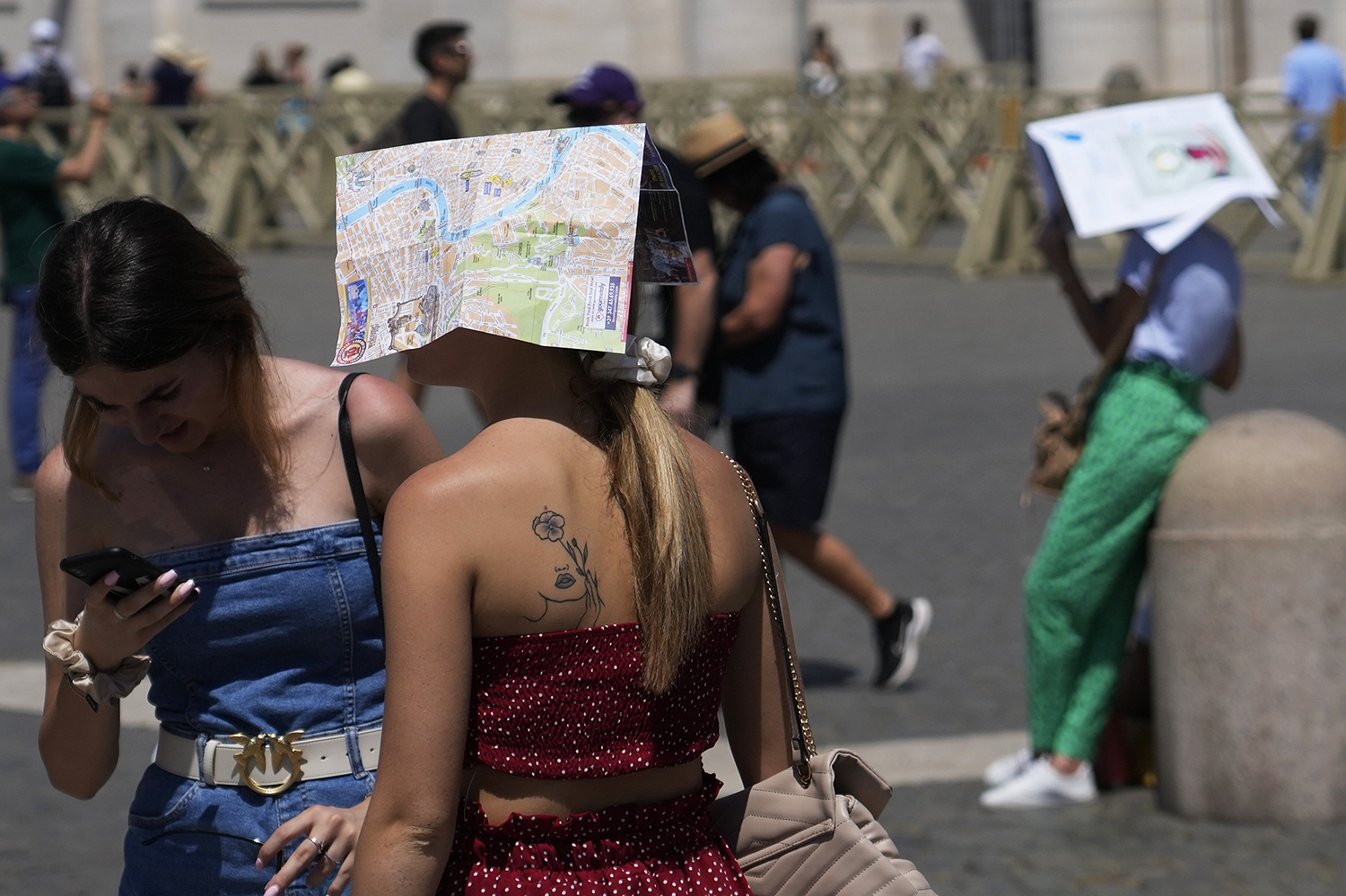 A tourist shelters with a Rome's map as he waits for the start of Pope Francis' Angelus noon prayer in St. Peter's Square at the Vatican, Sunday, July 9, 2023. (AP Photo/Gregorio Borgia)
