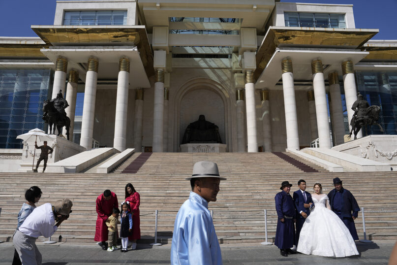 A family and a wedding couple pose for photos in front of the Government Palace, also known as State Palace, in Ulaanbaatar, capital of Mongolia, on Aug. 28, 2023. (AP Photo/Ng Han Guan)