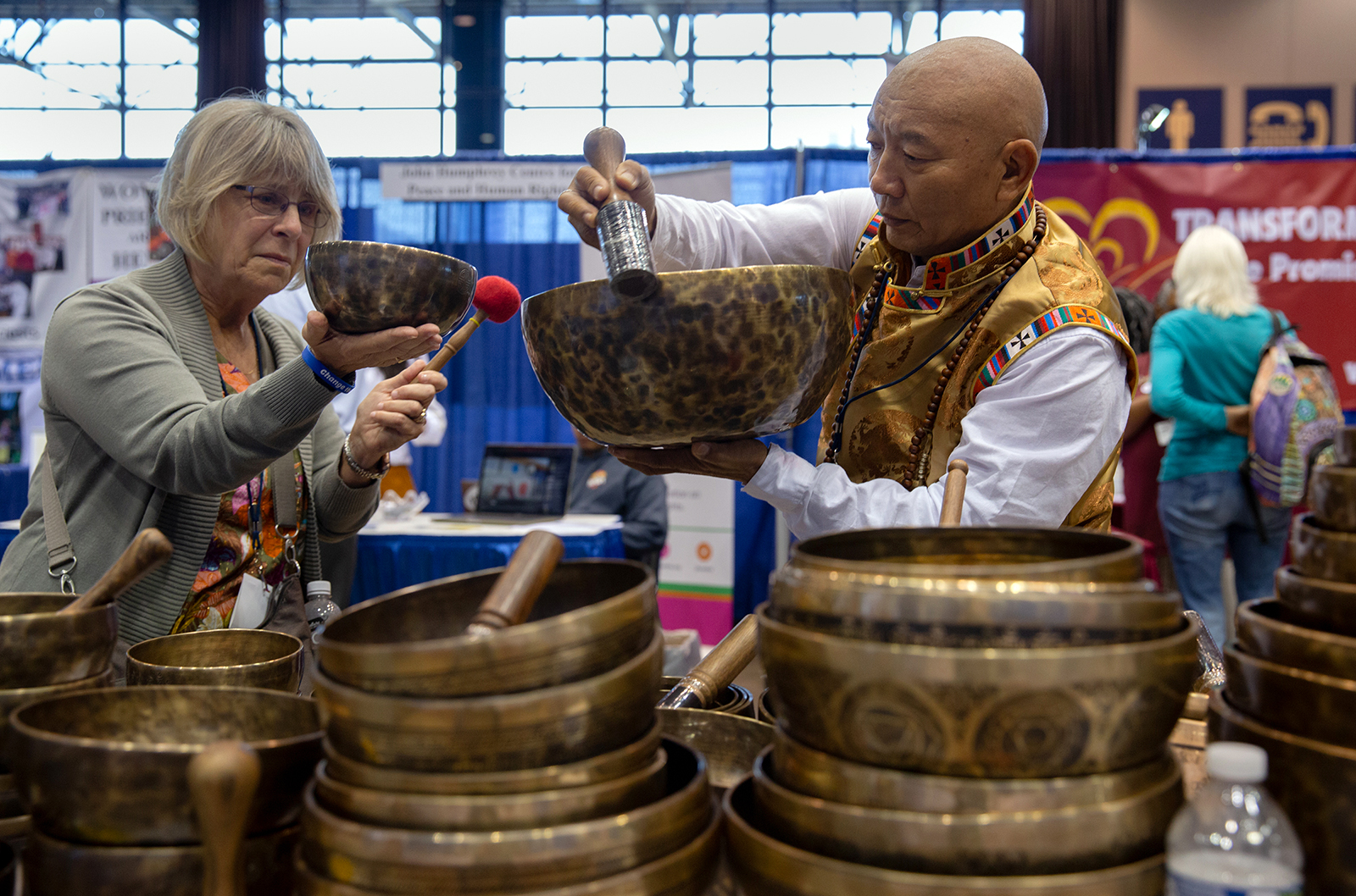 Jonor Lama, right, demonstrates the vibrations of singing bowls for Diane Maltester, left, in the exhibit hall of the Parliament of the World's Religions in Chicago on August 15, 2023. Maltester, a classical clarinetist, said she was interested in incorporating singing bowls into her music. Photo by Lauren Pond for RNS