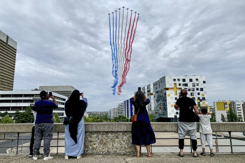 Residents watch French air force jets fly over a Paris suburb during the Bastille Day military parade on July 14, 2023. (AP Photo/Youcef Bounab)