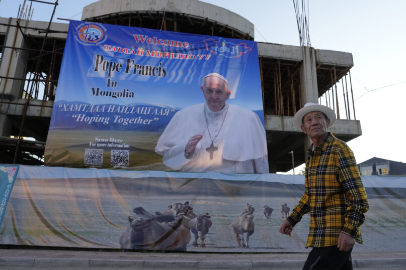 A Mongolian man walks past a banner promoting the visit of Pope Francis near a church in Ulaanbaatar, Mongolia on Monday, Aug. 28, 2023. (AP Photo/Ng Han Guan)