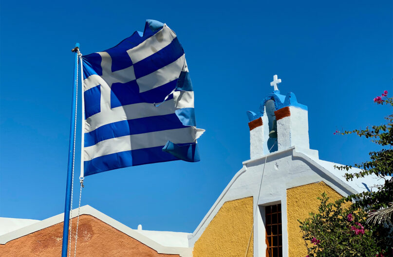 The Greek flag flies outside a Greek Orthodox Church in Santorini, Greece. Photo by iSAW Company/Unsplash/Creative Commons