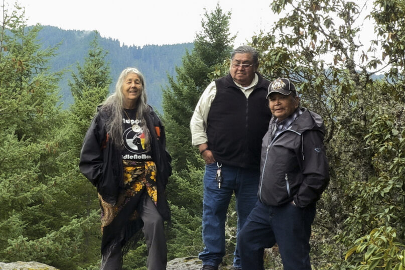CAPTION ADDITION ADDS LOCATION AND DATE: In this photo provided by Madeline Hartman, Carol Logan, left, Wilbur Slockish, center, and Johnny Jackson stand on Enola Hill on Mount Hood, Ore., in 2015. Slockish, Logan and Jackson were plaintiffs in a 2008 lawsuit filed against the U.S. Department of Transportation over damage to a site sacred to local tribes along U.S. Highway 26 on Mount Hood. The U.S. government has agreed to help restore the sacred Native American site on the slopes of Oregon's Mount Hood that was destroyed by highway construction, court documents show, capping more than 15 years of legal battles that went all the way to the U.S. Supreme Court. (Madeline Hartman via AP)