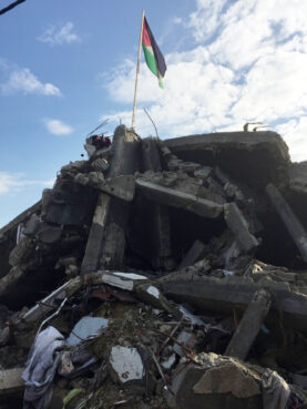 A Palestinian flag stands amidst the rubble of a destroyed building in Gaza in 2014. Photo by Aura Kanegis