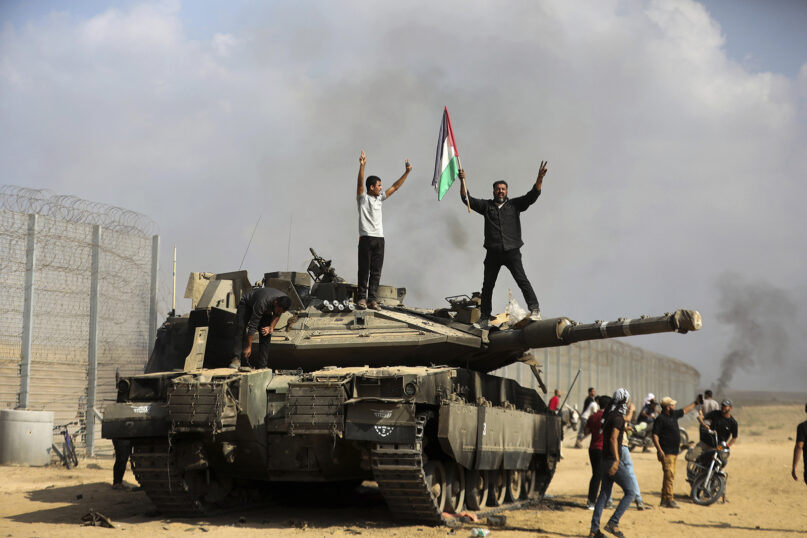 Palestinians wave their national flag and celebrate by a destroyed Israeli tank at the southern Gaza Strip fence east of Khan Younis, Oct. 7, 2023. (AP Photo/Yousef Masoud)