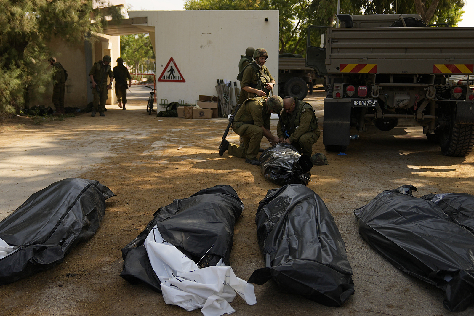 Israeli soldiers stand next to the bodies of Israelis killed by Hamas militants in kibbutz Kfar Azza on Tuesday, Oct. 10, 2023. Hamas militants overran Kfar Azza on Saturday, where many Israelis were killed and taken captive. (AP Photo/Ohad Zwigenberg)
