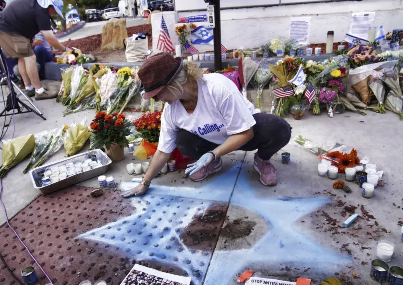 Elena Colombo chalks a Star of David on Nov. 7, 2023, in Thousand Oaks, Calif., alongside flowers and candles left at a makeshift shrine placed at the scene of a confrontation that led to a death of a demonstrator. California authorities have arrested a man in connection with the death during demonstrations Nov. 5, 2023, over the Israel-Hamas war. (AP Photo/Richard Vogel)