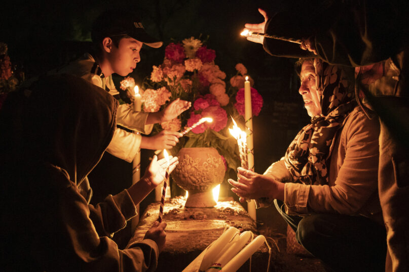 People hold candles over a tomb decorated with flowers at a cemetery in Atzompa, Mexico, late Tuesday, Oct. 31, 2023. In a tradition that coincides with All Saints Day on Nov. 1 and All Souls Day on Nov. 2, families decorate graves with flowers and candles and spend the night in the cemetery, eating and drinking as they keep company with their dearly departed. (AP Photo/Maria Alferez)