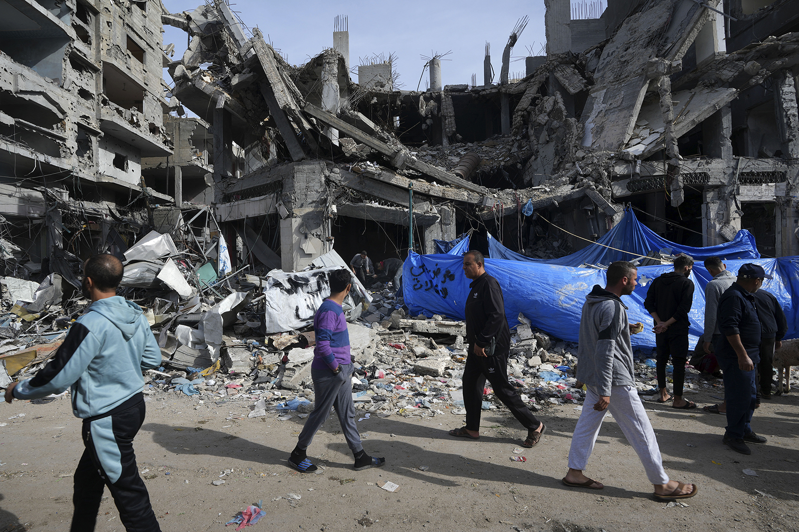 Palestinians walk by buildings destroyed in the Israeli bombardment of the Gaza Strip in Nuseirat refugee camp, central Gaza Strip, Nov. 25, 2023, on the second day of the temporary cease-fire between Hamas and Israel. (AP Photo/Adel Hana)