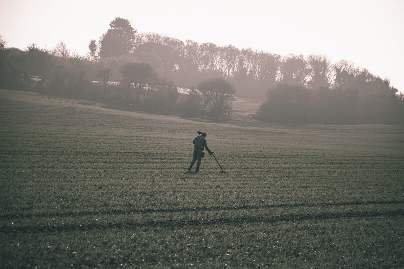 An individual uses a metal detector in a field. (Photo by Jack B/Unsplash/Creative Commons)