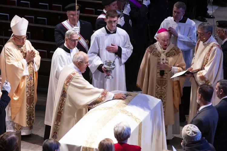 Deacon Paul Cerio places a cross on the casket of Rev. Stephen Gutgsell during his funeral at St. Cecilia Cathedral in Omaha, Neb., on Monday, Dec. 18, 2023. Gutsgell was killed in the rectory of St. John the Baptist Church in Fort Calhoun on Dec. 10.