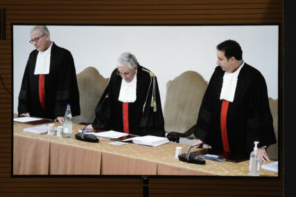 A screen shows Vatican tribunal president Giuseppe Pignatone reading the verdict of a trial against Cardinal Angelo Becciu and nine other defendants, in the Vatican press room, Saturday, Dec. 16, 2023. A once-powerful cardinal and nine other people are to learn their fates when a Vatican tribunal hands down verdicts in a complicated financial trial that has aired the tiny city state's dirty laundry. Judge Giuseppe Pignatone will read out the verdicts of the three-judge panel in the converted courtroom in the Vatican Museums on Saturday. (AP Photo/Andrew Medichini)