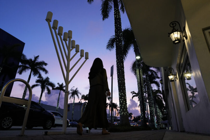 A woman in conservative dress walks past a menorah standing outside a Jewish synagogue ahead of the start of Hanukkah, in Miami Beach, Fla., Friday, Dec. 1, 2023. Daily life for many Jews has been upended by the surprise attack on Oct. 7 in Israel, when Hamas militants killed about 1,200, mostly civilians, and by the rise in antisemitism worldwide during the ensuing war, in which more than 15,800 Palestinians have died. (AP Photo/Rebecca Blackwell)