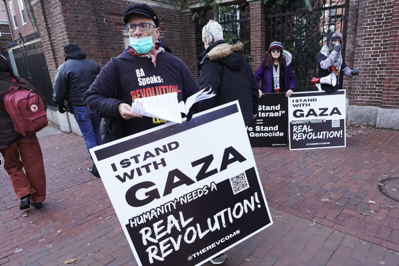 George Stevens, of Cambridge, Mass., front, hands out leaflets to passers-by near an entrance to Harvard University, Tuesday, Dec. 12, 2023, in Cambridge, while joining with pro-Palestinian demonstrators during a protest held to call for an end to the war in Gaza. Harvard President Claudine Gay will remain leader of Harvard following her comments last week at a congressional hearing on antisemitism, the university's highest governing body announced Tuesday. (AP Photo/Steven Senne)