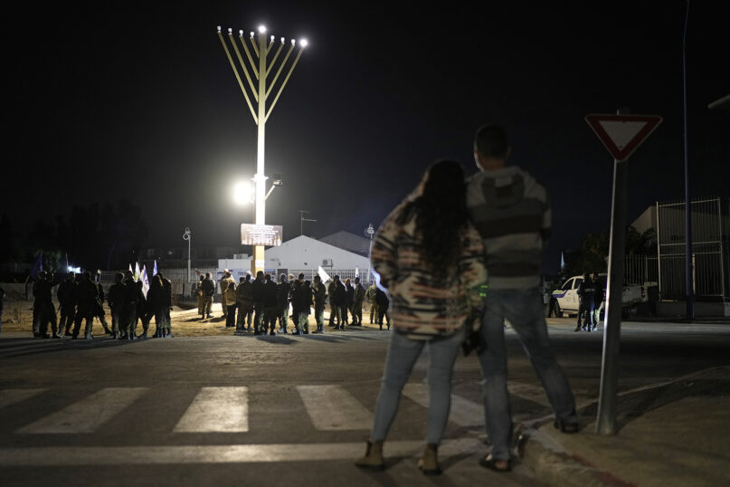 People gather around a menorah lit up for Hanukkah, placed at the former site of a police station that was overrun by Hamas militants on Oct. 7, in Sderot, southern Israel, Thursday Dec. 7, 2023. (AP Photo/Leo Correa)