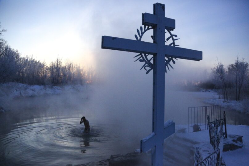 FILE - A man crosses himself while bathing in the water during a traditional Epiphany celebration as the temperature dropped to about -24 degrees (-11,2 degrees Fahrenheit) near the Achairsky monastery outside Siberian city of Omsk, Russia, Tuesday, Jan. 19, 2021. Water that is blessed by a cleric on Epiphany is considered holy and pure until next year's celebration, and is believed to have special powers of protection and healing. The Russian Orthodox Church follows the old Julian calendar.. (AP Photo/Evgeniy Sofiychuk, File)