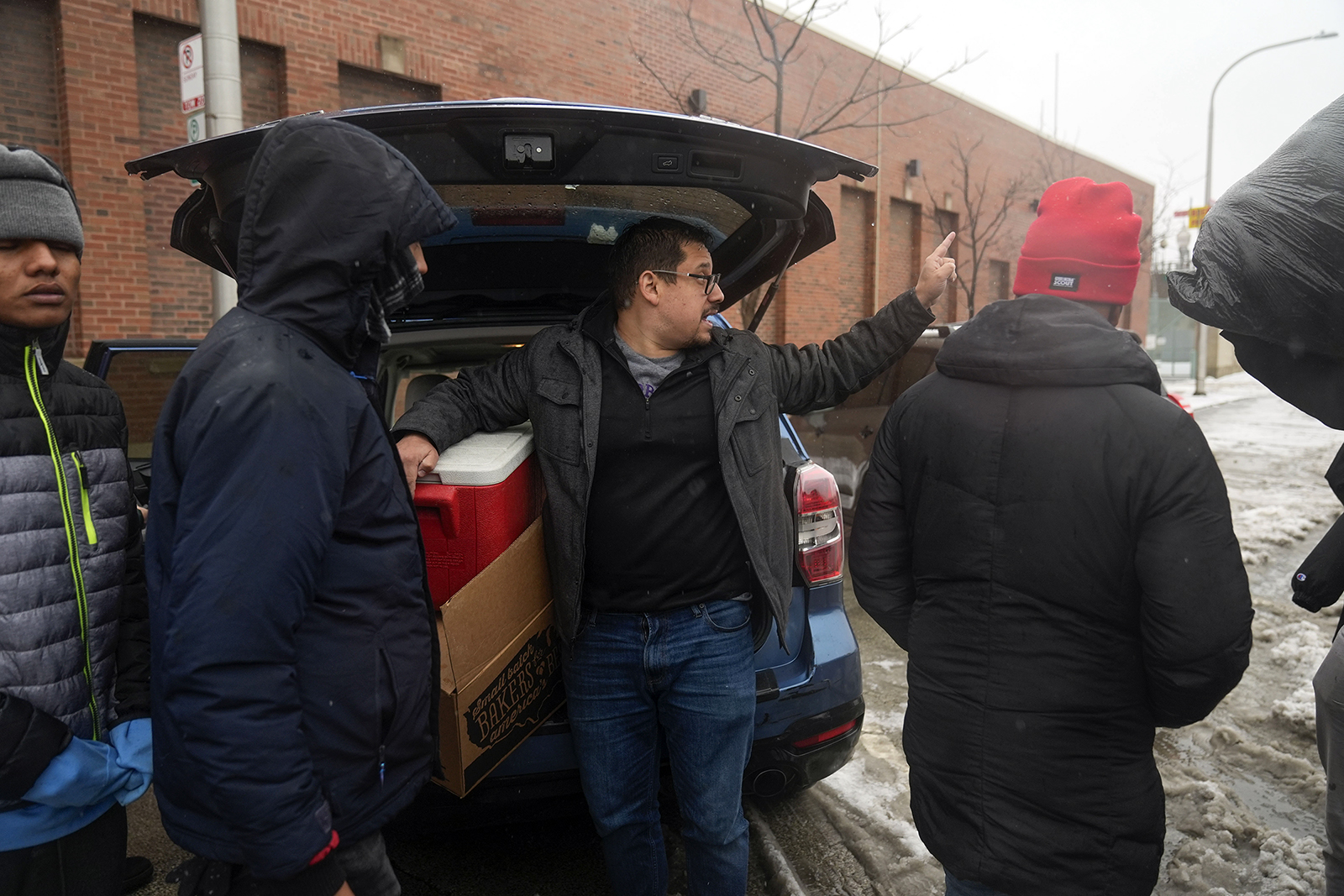 Pastor Jonathan de la O, of Starting Point Community Church, instructs migrants to meet him down the street to receive food and clothing donations after Chicago police officers, citing safety concerns, told him they didn't want migrants crossing the street from where "warming" buses are parked in the 800 block of South Desplaines Street as a winter storm passes through Friday, Jan. 12, 2024, in Chicago. In the city of Chicago's latest attempt to provide shelter to incoming migrants, several buses were parked in the area to house people in cold winter weather. (AP Photo/Erin Hooley)
