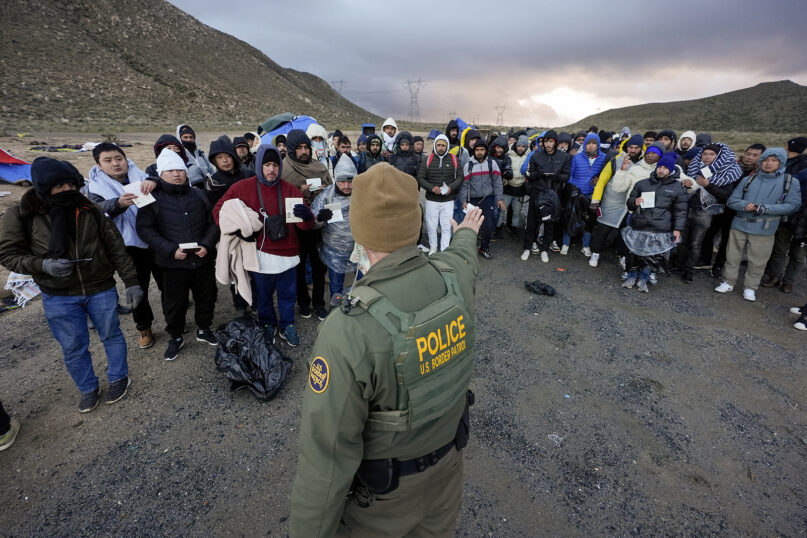 A Border Patrol agent asks asylum-seeking migrants to line up in a makeshift, mountainous campsite after the group crossed the border with Mexico, Feb. 2, 2024, near Jacumba Hot Springs, Calif. (AP Photo/Gregory Bull)