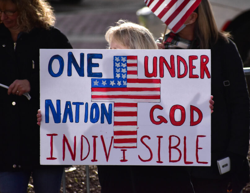An attendee holds a “One Nation Under God Indivisible” poster during a Stop the Steal protest in Raleigh, N.C., on Jan. 6, 2021. (Photo by Anthony Crider/Flickr/CC-BY 2.0)