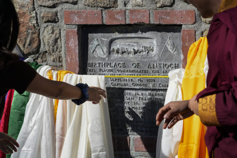 Buddhist faith leaders and community members drape Tibetan prayer scarves on the Birthplace of Antioch marker during the 