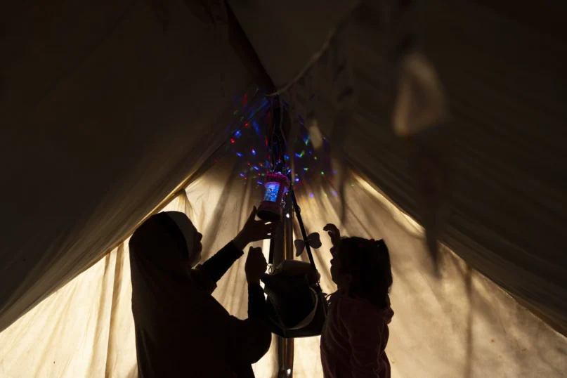 Randa Baker, who was displaced by the Israeli bombardment of the Gaza Strip, hangs Ramadan decorations and lanterns with her daughter, remarking the beginning of the Muslim holy fasting month of Ramadan at a makeshift tent camp in the Muwasi area, southern Gaza, March 11, 2024. (AP Photo/Fatima Shbair)