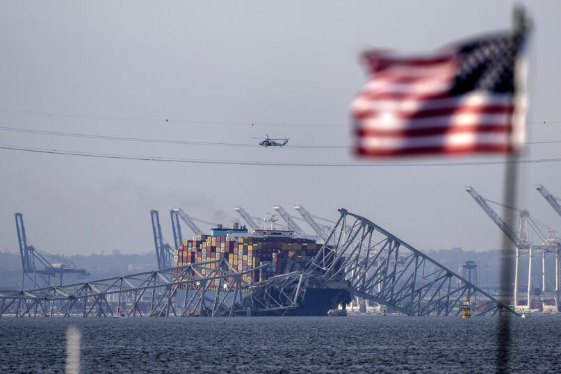 An American flag flies on a moored boat as the container ship Dali rests against wreckage of the Francis Scott Key Bridge, March 26, 2024, as seen from Pasadena, Md. (AP Photo/Mark Schiefelbein)