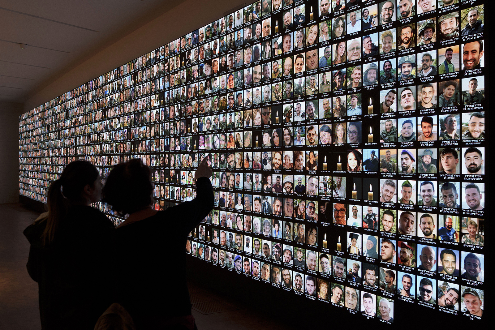 FILE - Visitors look at photos of Israeli people who were killed during the Hamas attack on Oct. 7 and those who died during the Israel-Hamas war in the Gaza Strip, displayed on a giant screen at the National Library in Jerusalem, Israel, Jan. 28, 2024. (AP Photo/Leo Correa, File)