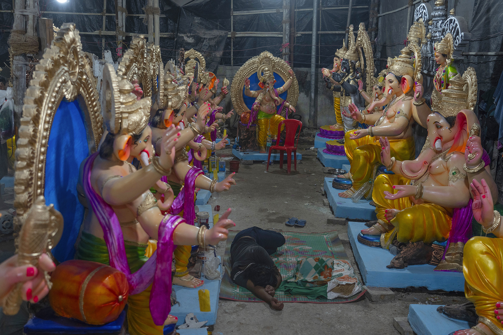 Um artista tira uma soneca durante uma pausa na criação de estátuas do deus hindu com cabeça de elefante Ganesha dentro de uma oficina antes do festival Ganesh Chaturthi em Mumbai, Índia, quarta-feira, 4 de setembro de 2024. (AP Photo/Rafiq Maqbool)